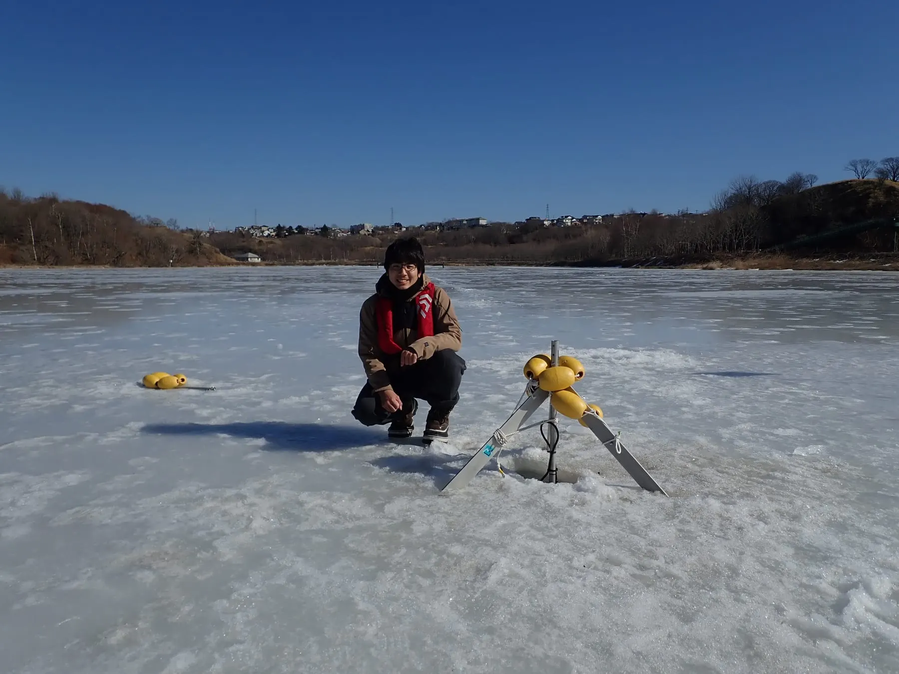結氷した湖の上で、氷に開けた穴のそばにしゃがみ、観測機器を設置しているところ