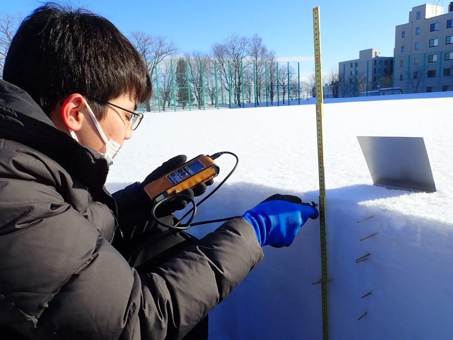 雪を掘って作った断面の前で、温度計を手に持ち、雪の中に挿した測点を読み取っているところ